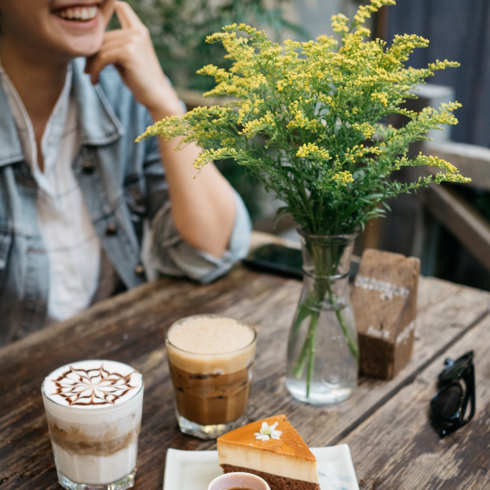 Eine lächelnde Person sitzt an einem Tisch und trinkt Kaffee.